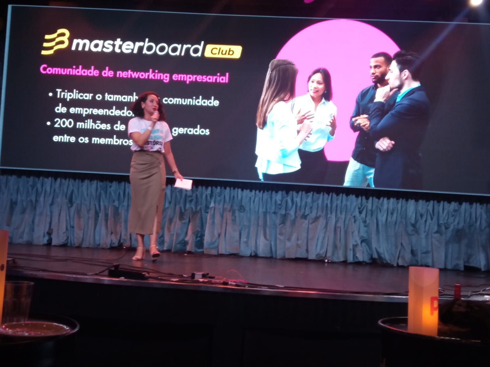 Uma mulher está em um palco em frente a uma tela que diz masterboard club