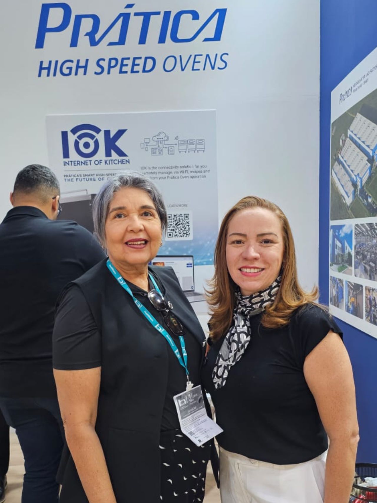 Duas mulheres sorriem, em frente a um expositor de fornos 