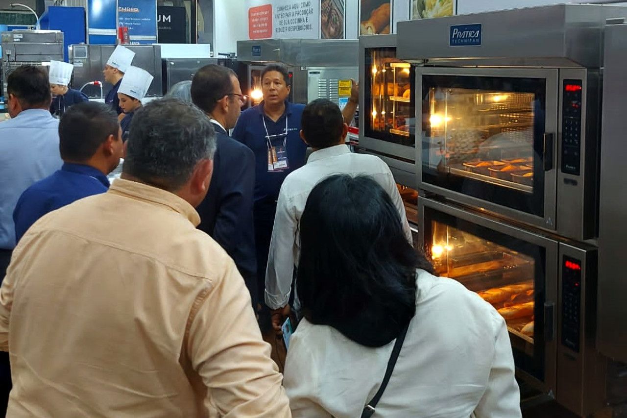 Um grupo de pessoas está em pé na frente de uma fileira de fornos