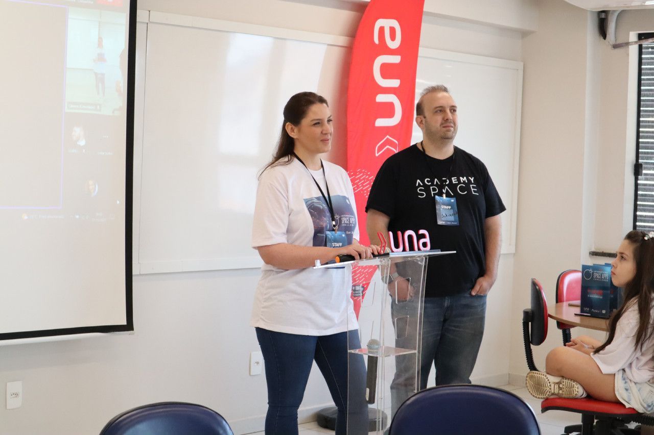 Um homem e uma mulher estão em pé na frente de um pódio em uma sala de aula.