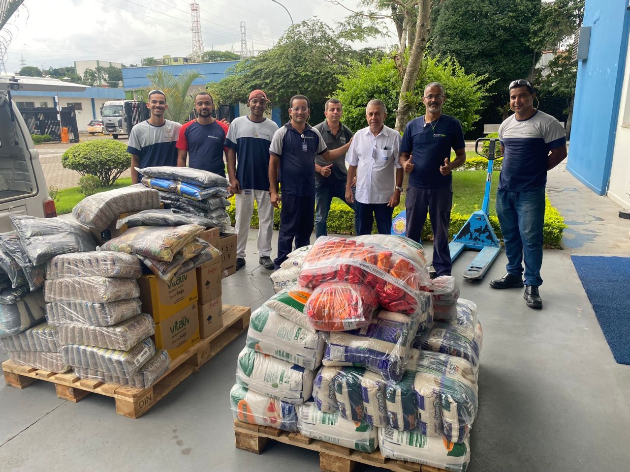 Um grupo de homens está em pé em frente a um palete de comida.