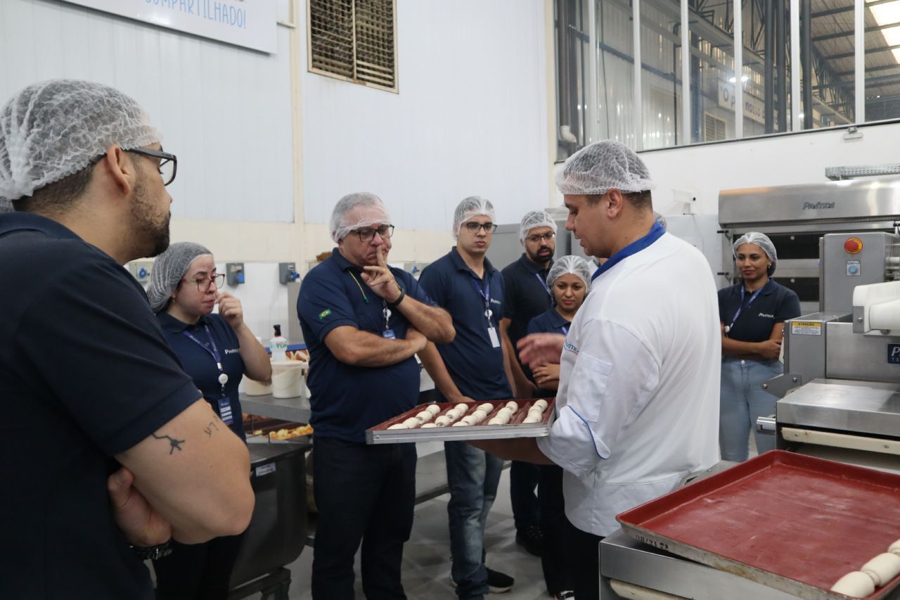 Um grupo de pessoas está em volta de um homem segurando uma bandeja de massa.