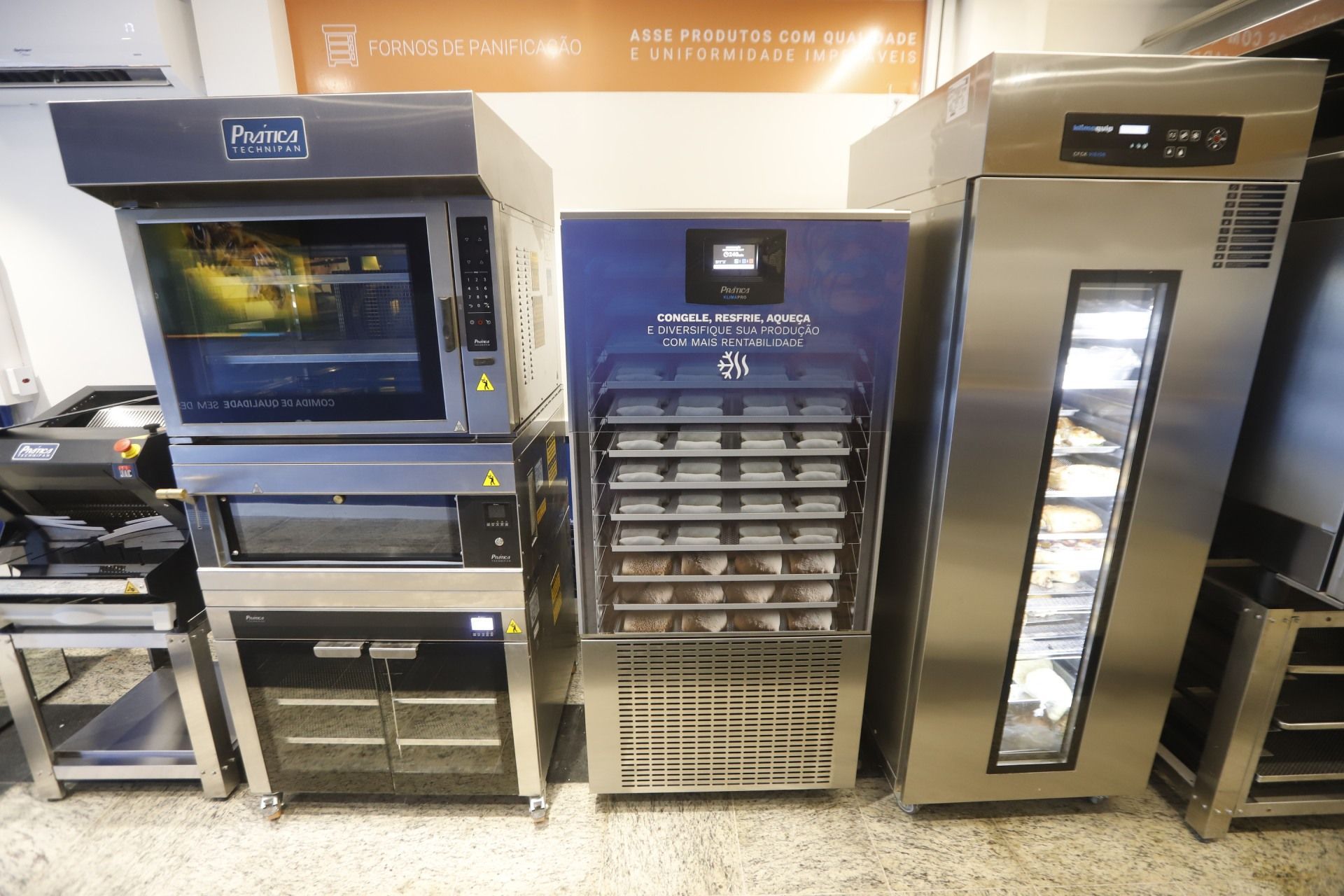 Eletrodomésticos de cozinha comercial, incluindo forno, freezer e fermentador, contra uma parede com texto.