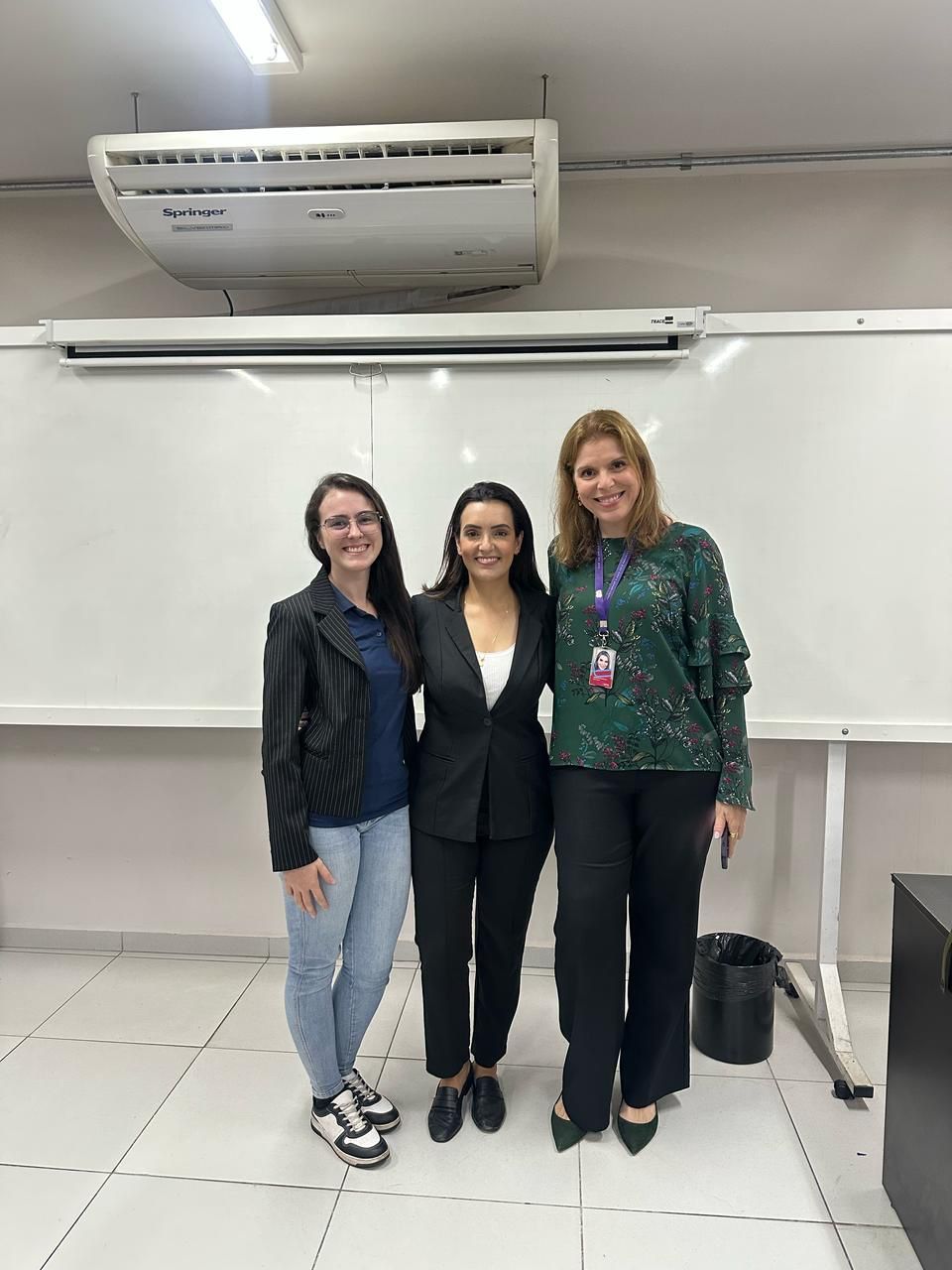 Três mulheres estão posando para uma foto em frente a um quadro branco.