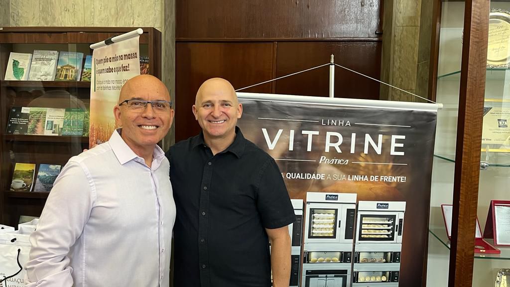 Dois homens estão posando para uma foto em frente a uma placa que diz vitrine.