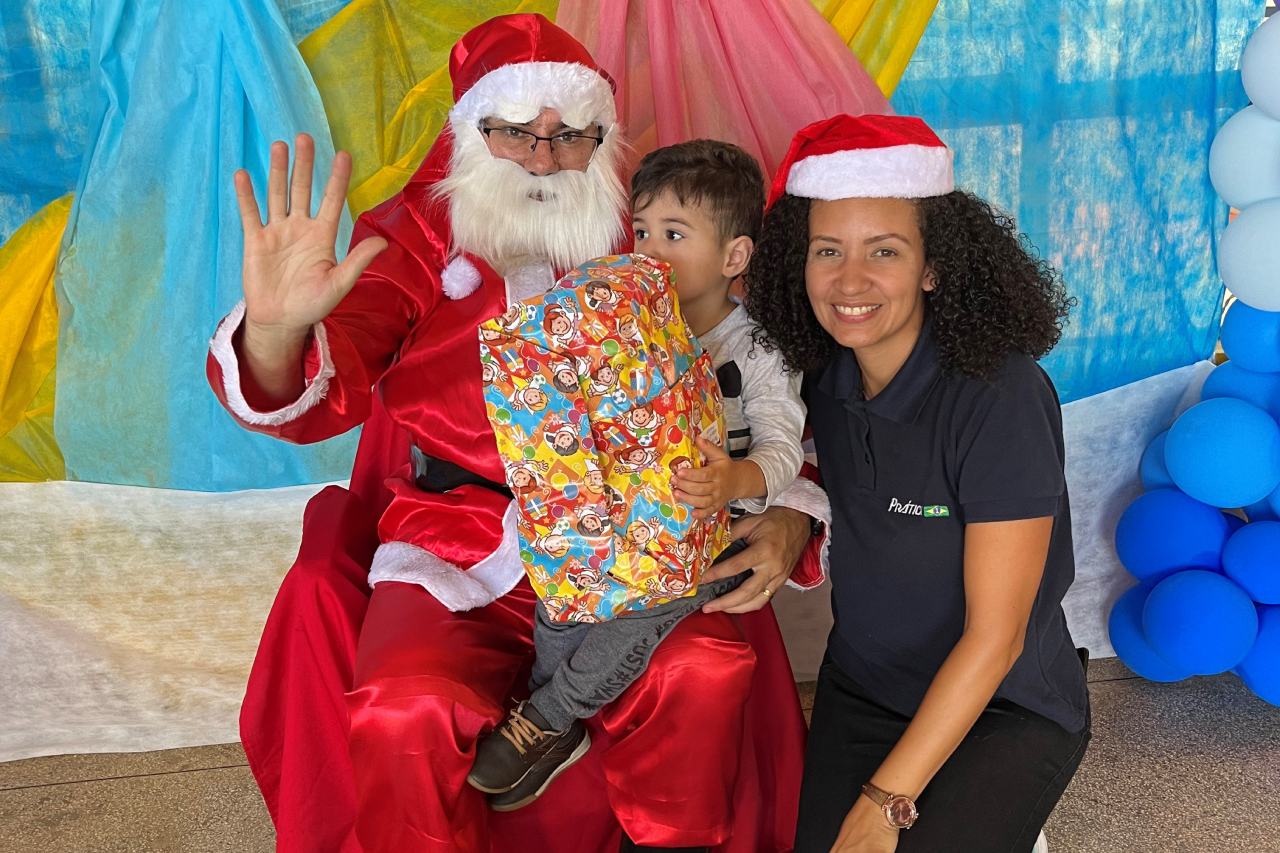 Uma mulher está ajoelhada ao lado de uma criança sentada no colo do Papai Noel.