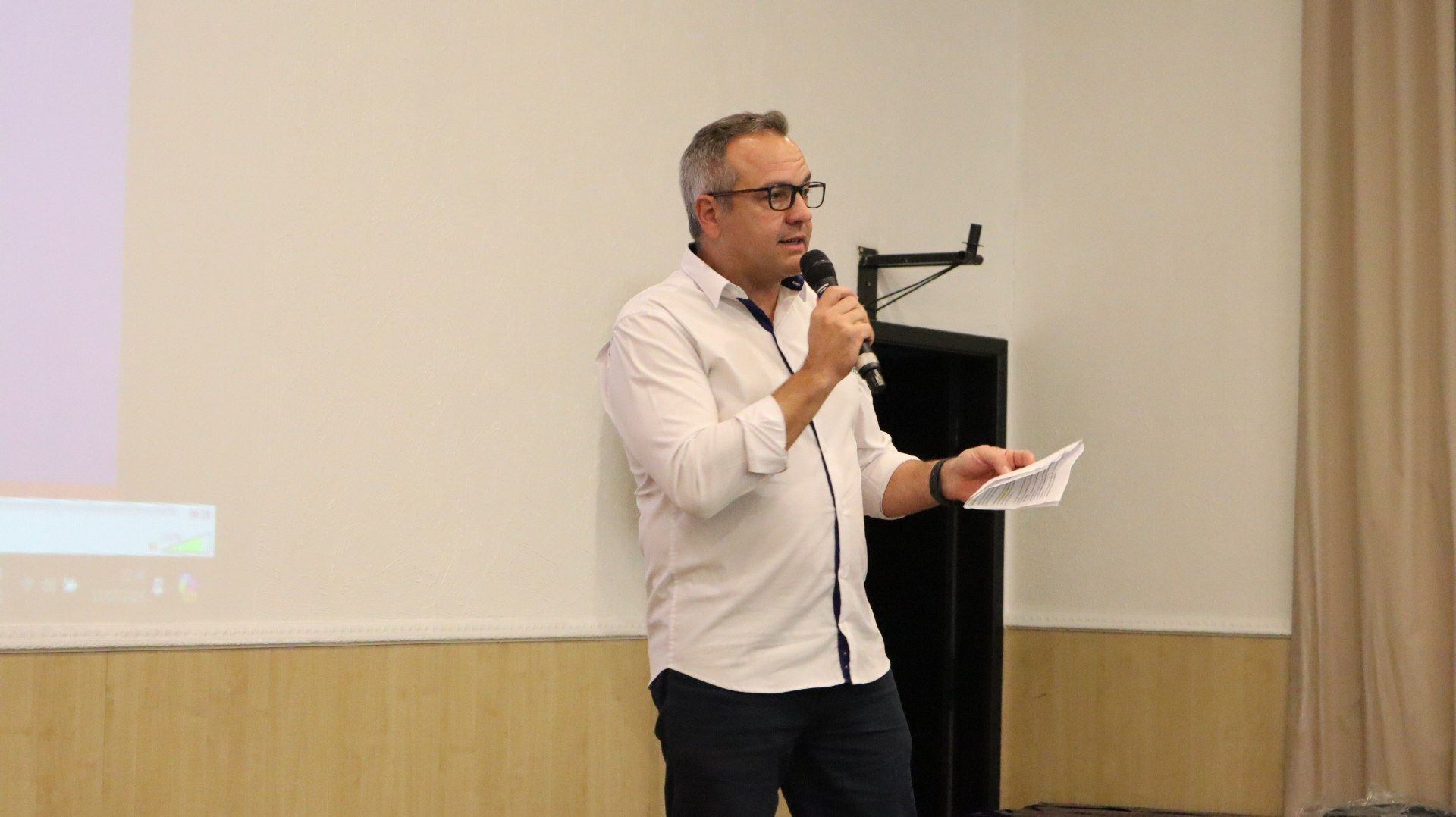 Um homem está em pé na frente de uma tela de projetor segurando um microfone.