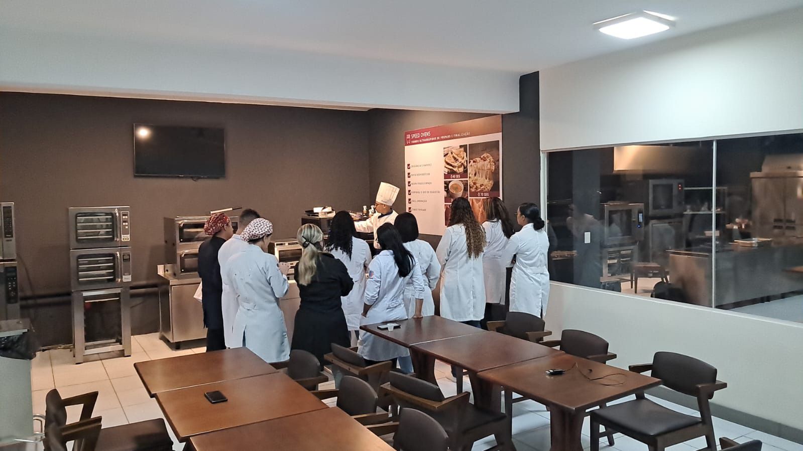 Um grupo de pessoas está de pé em uma sala com mesas e cadeiras.