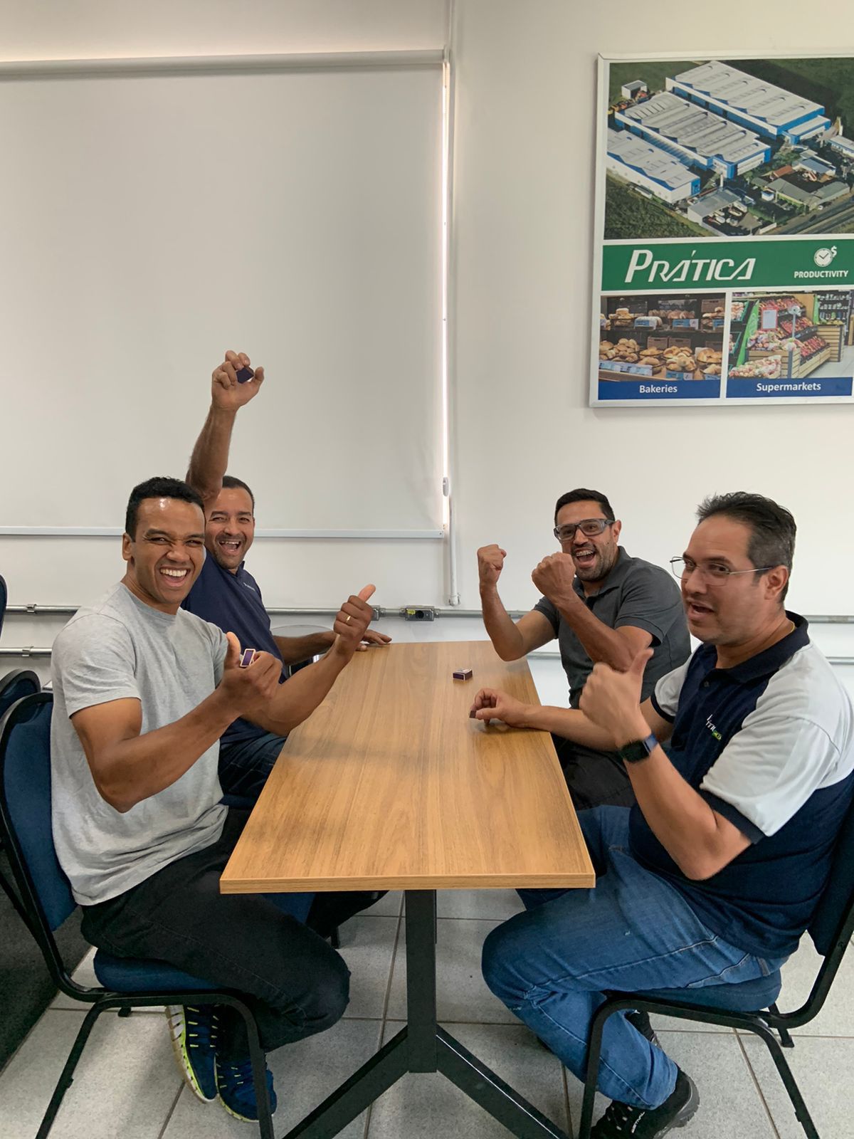 Um grupo de homens está sentado à mesa com as mãos no ar.