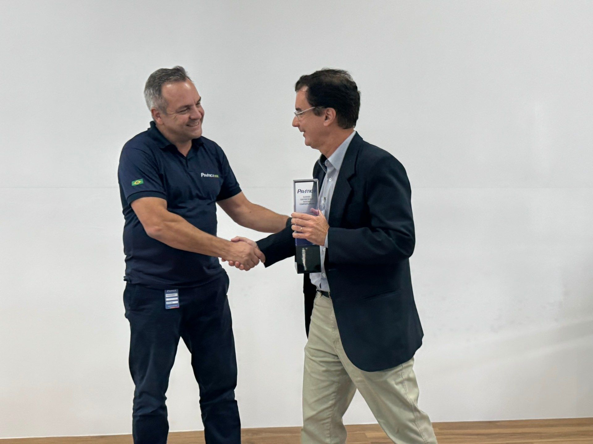 Dois homens apertam as mãos em frente a uma parede branca.