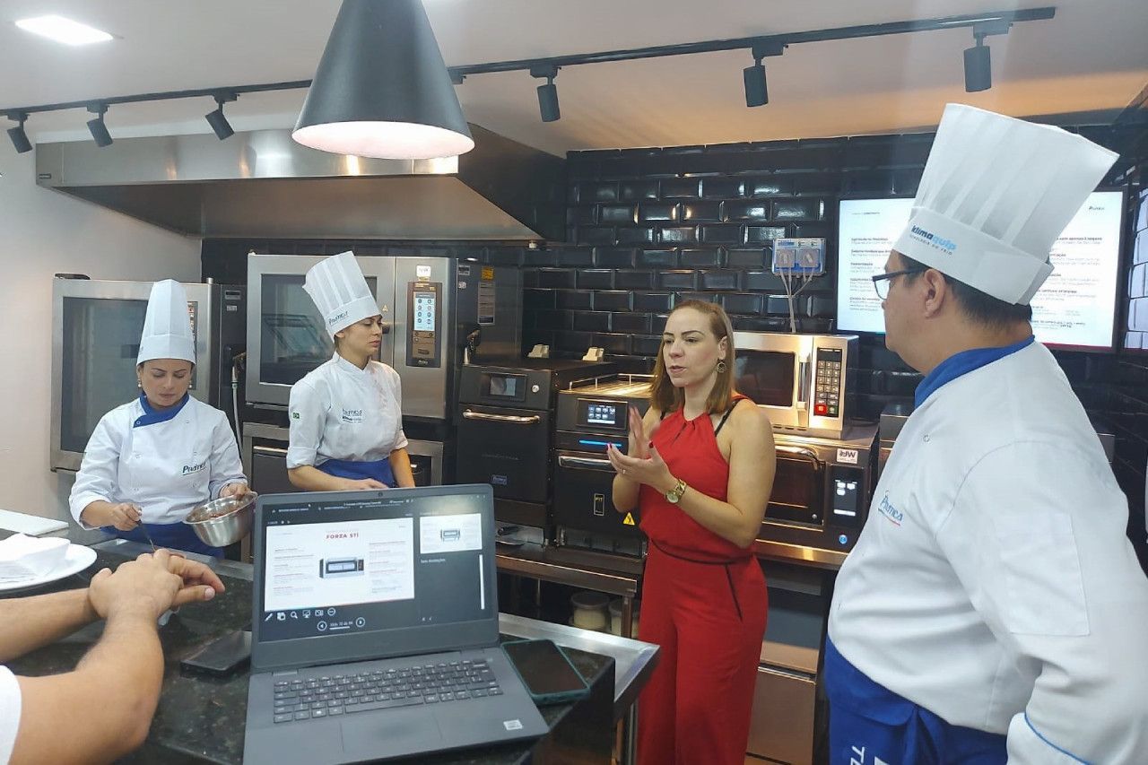 Um grupo de chefs está em volta de um laptop em uma cozinha.