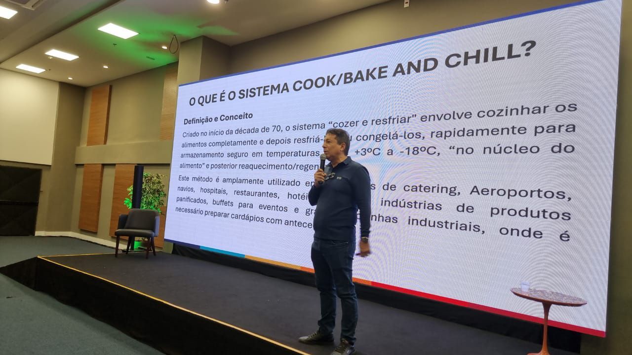 Um homem está fazendo uma apresentação em frente a uma tela grande.