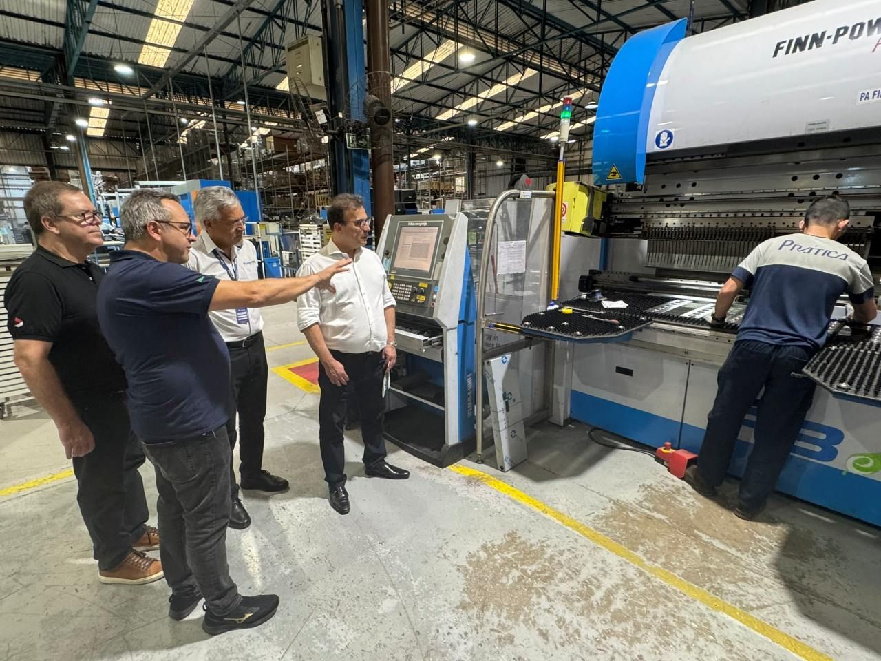 Um grupo de homens está em volta de uma máquina em uma fábrica.