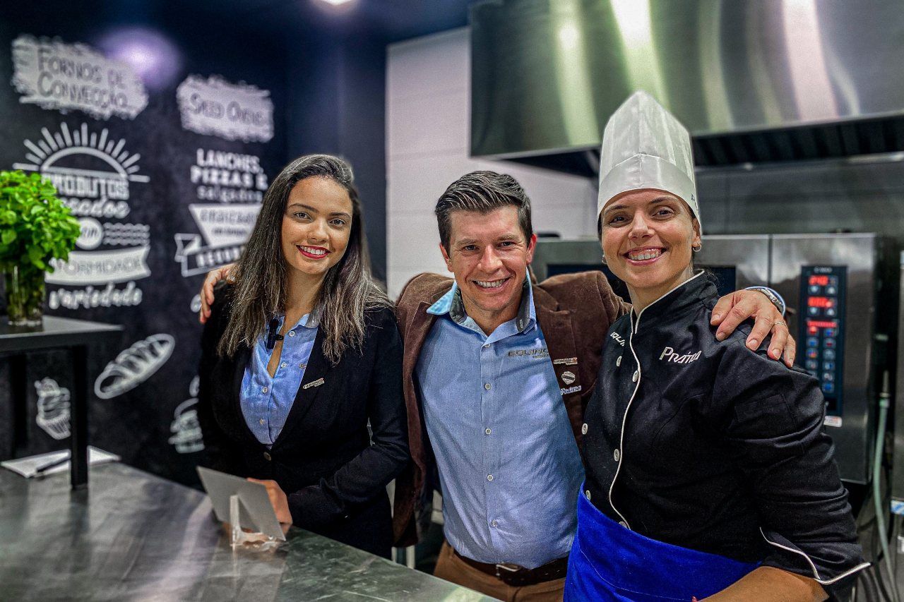 Um homem e duas mulheres estão posando para uma foto em uma cozinha.