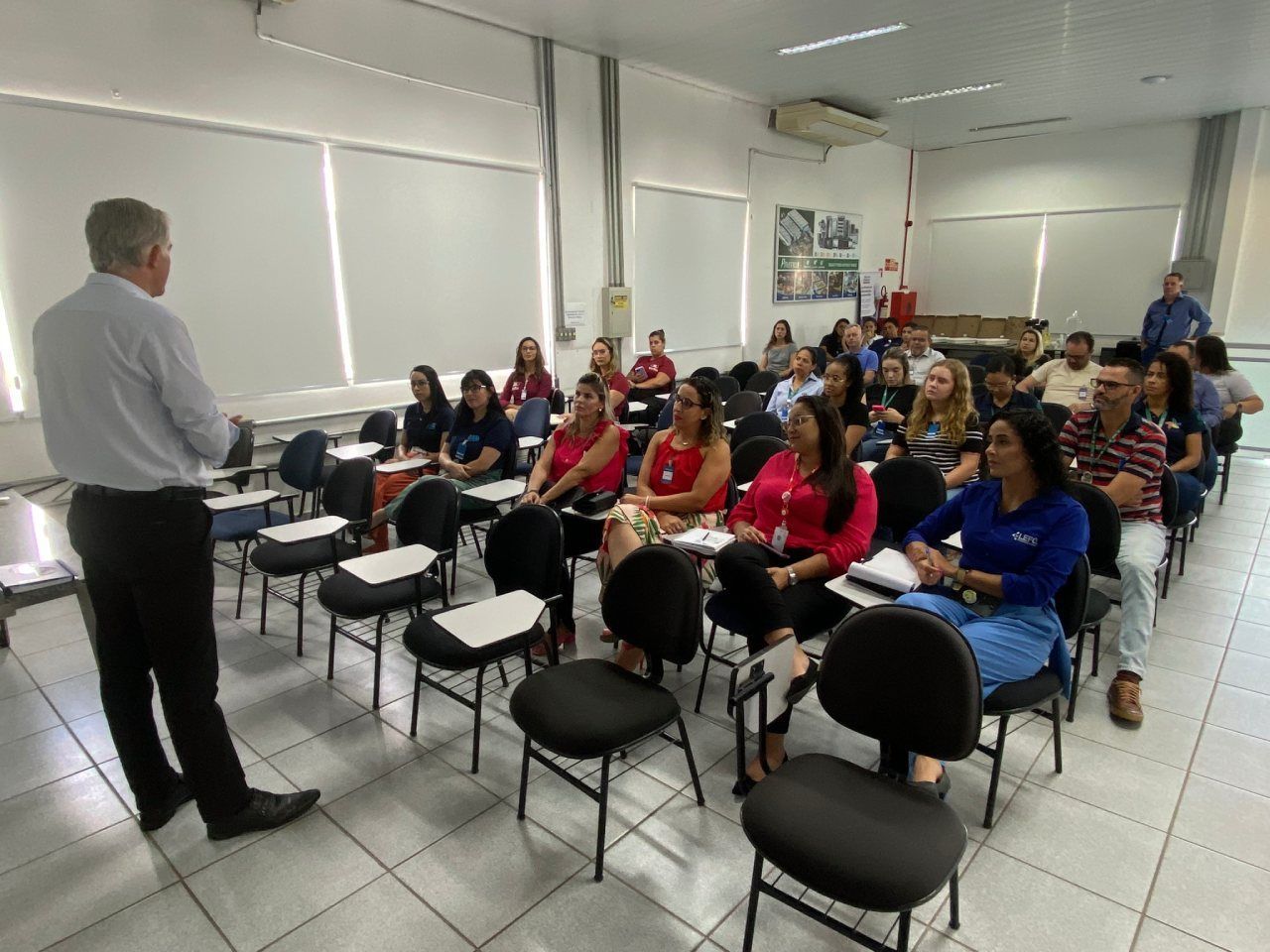 Um homem está fazendo uma apresentação para um grupo de pessoas sentadas em cadeiras em uma sala de aula.