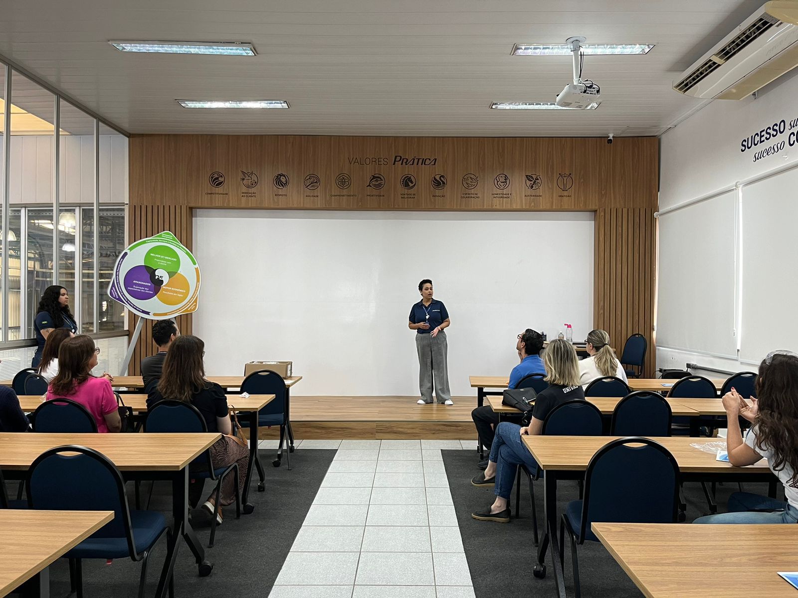 Um homem está em pé no palco em frente a um grupo de pessoas em uma sala de aula.