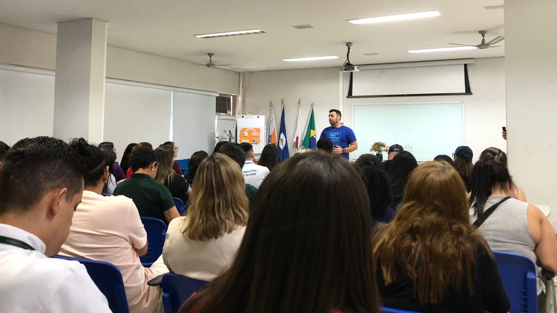 Um grupo de pessoas está sentado em uma sala assistindo a uma apresentação.