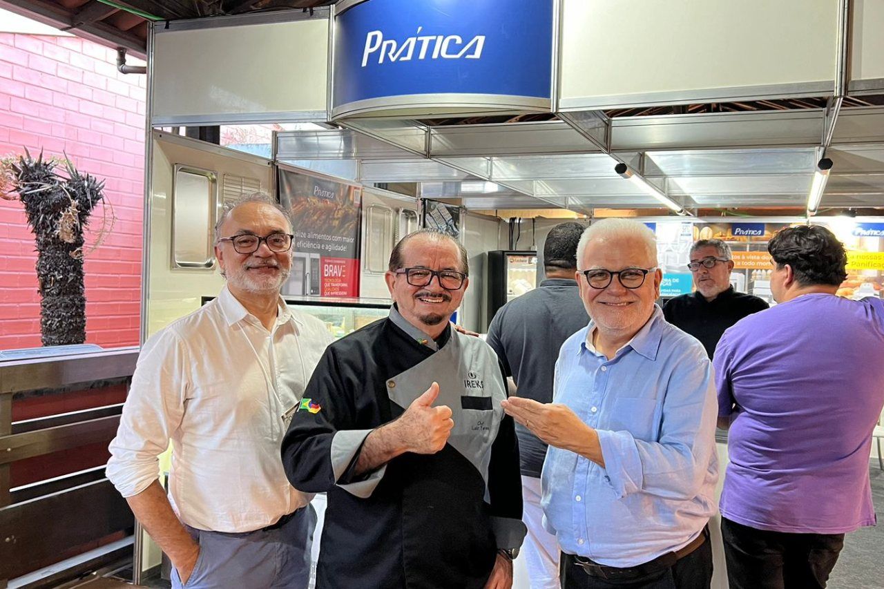 Três homens estão de pé, um ao lado do outro, em um restaurante, fazendo sinal de positivo.