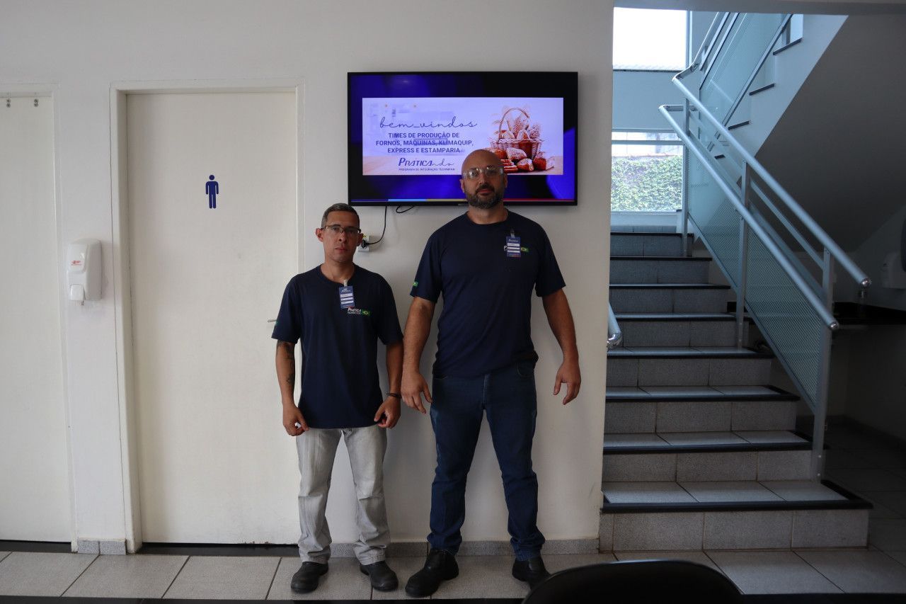 Dois homens parados um ao lado do outro em frente a uma televisão