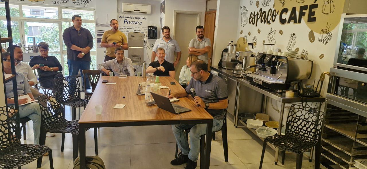 Um grupo de homens está sentado em uma longa mesa em um café.