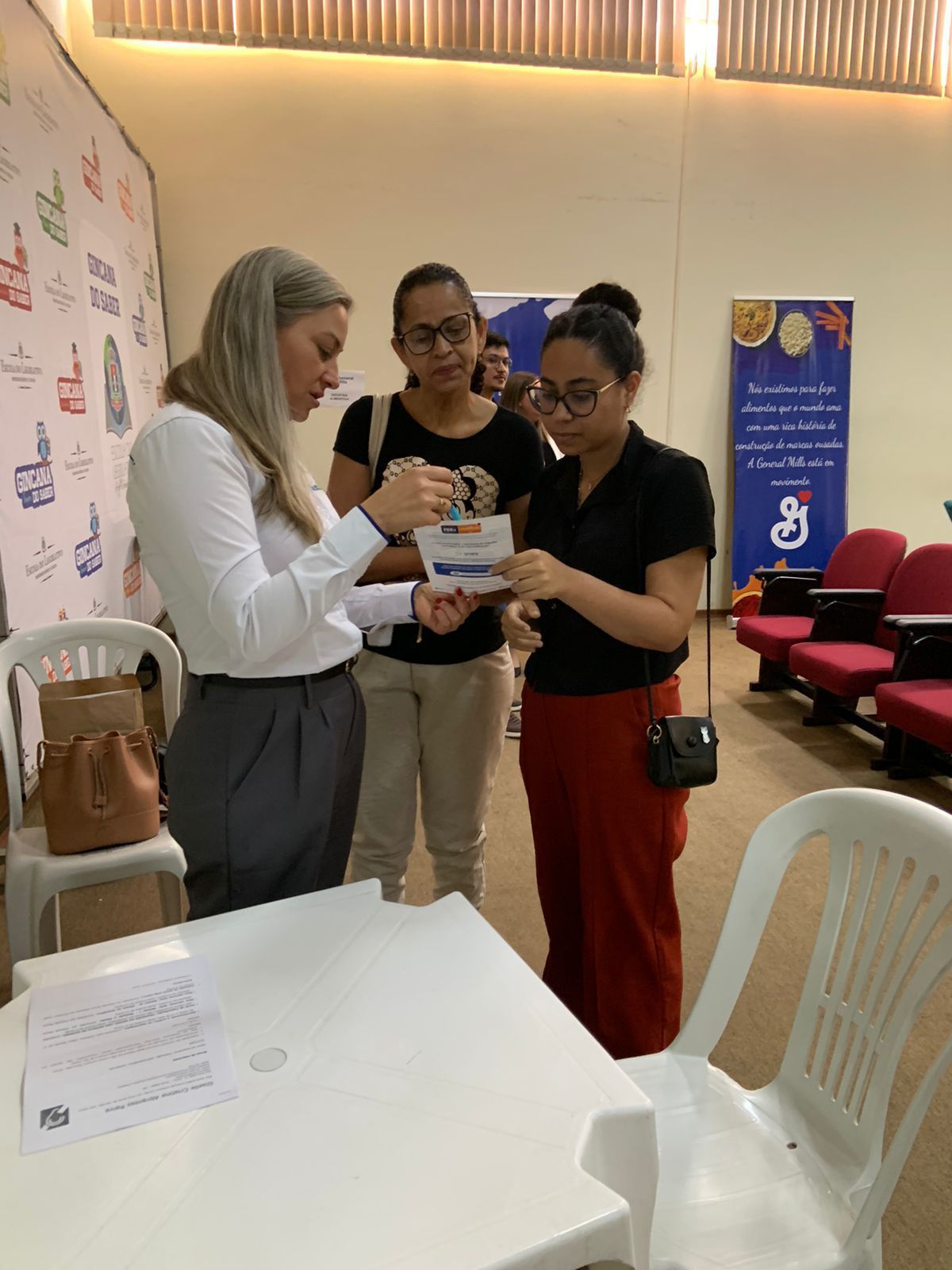 Três mulheres estão em pé ao redor de uma mesa olhando para um pedaço de papel.