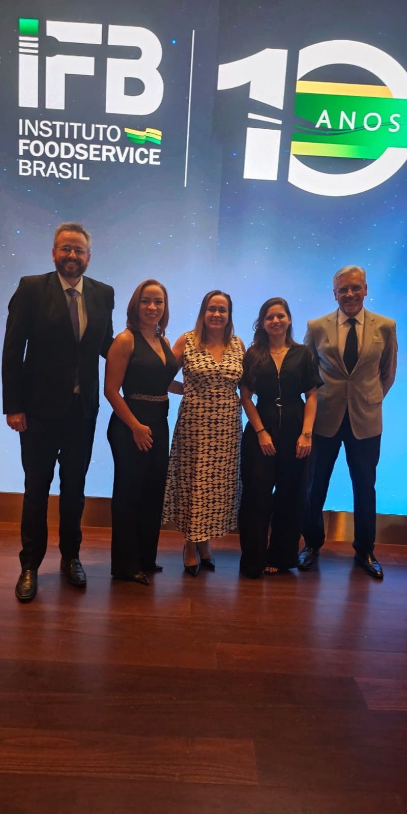 Um grupo de pessoas está posando para uma foto em frente a uma tela grande.