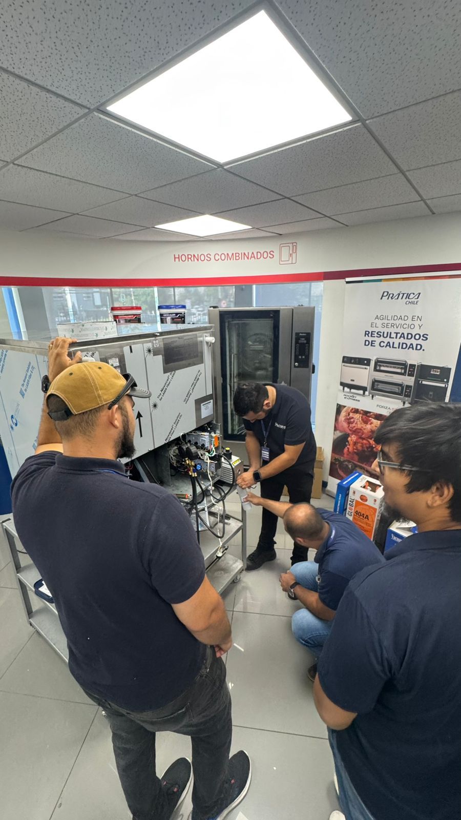Um grupo de pessoas está reunido em torno de uma máquina de aço inoxidável dentro de uma sala bem iluminada.