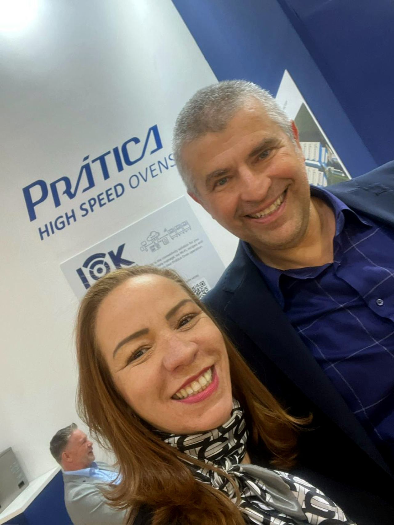 Mulher e homem sorrindo, tirando uma selfie em um estande da 