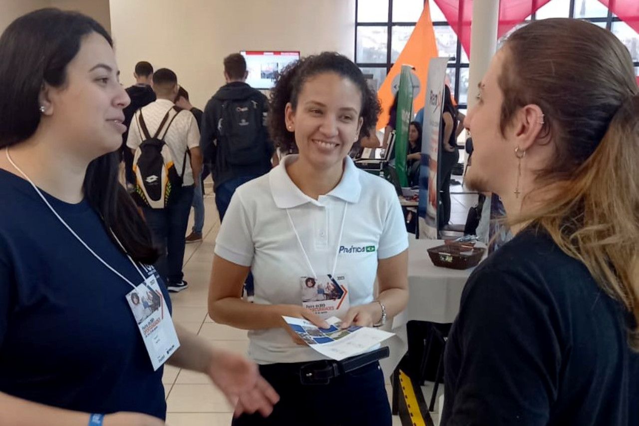 Uma mulher com uma camisa polo branca está conversando com outras duas mulheres