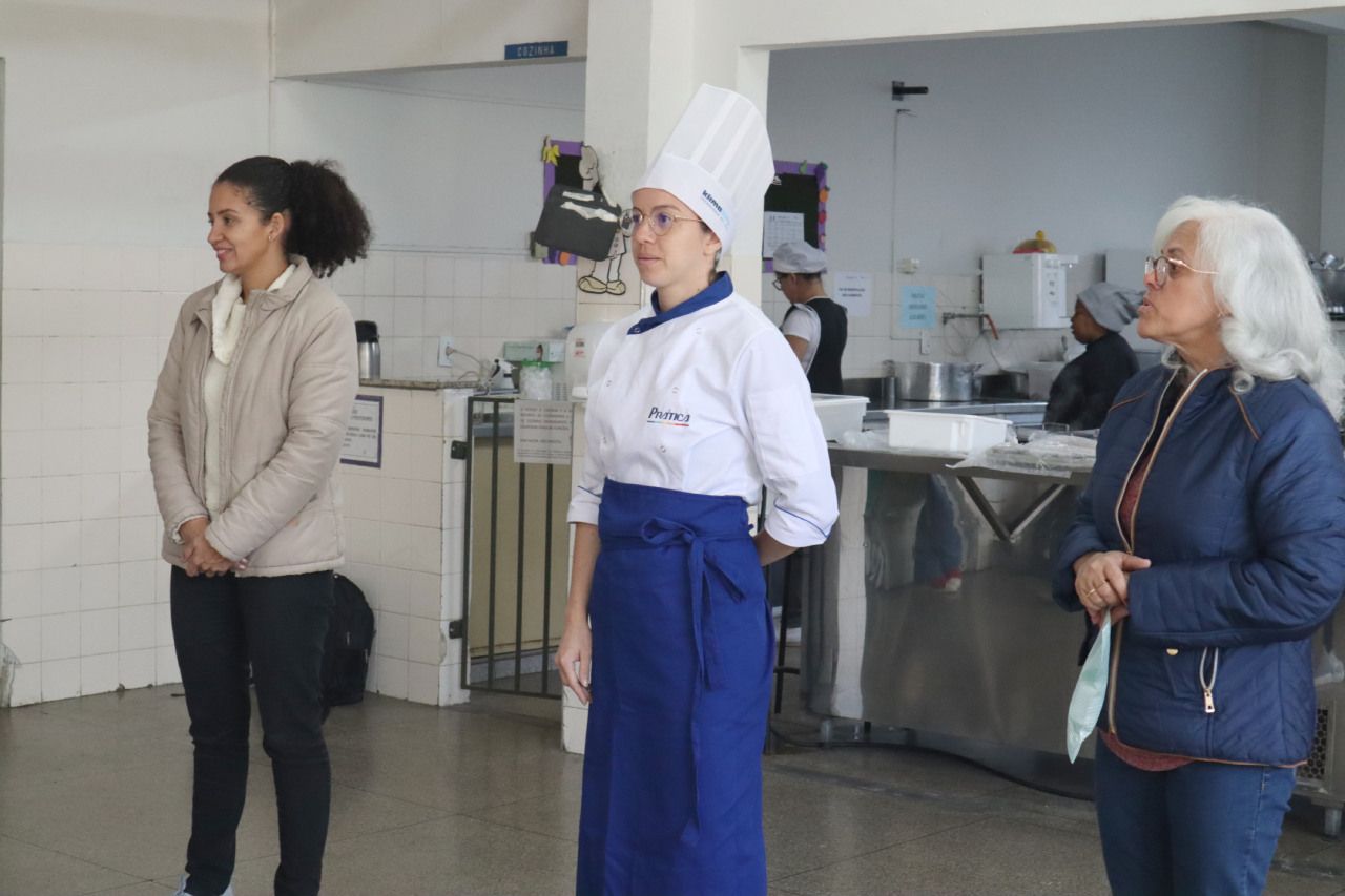 Uma mulher com chapéu de chef está parada ao lado de outras duas mulheres
