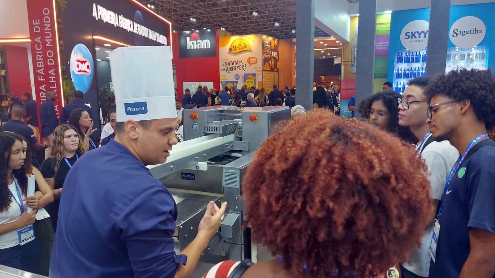 Um homem com chapéu de chef está conversando com um grupo de pessoas.