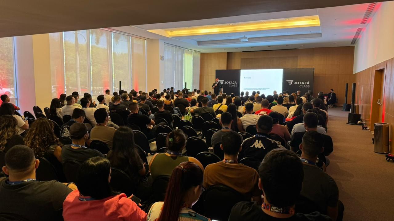 Um grande grupo de pessoas está sentado em uma sala grande assistindo a uma apresentação.