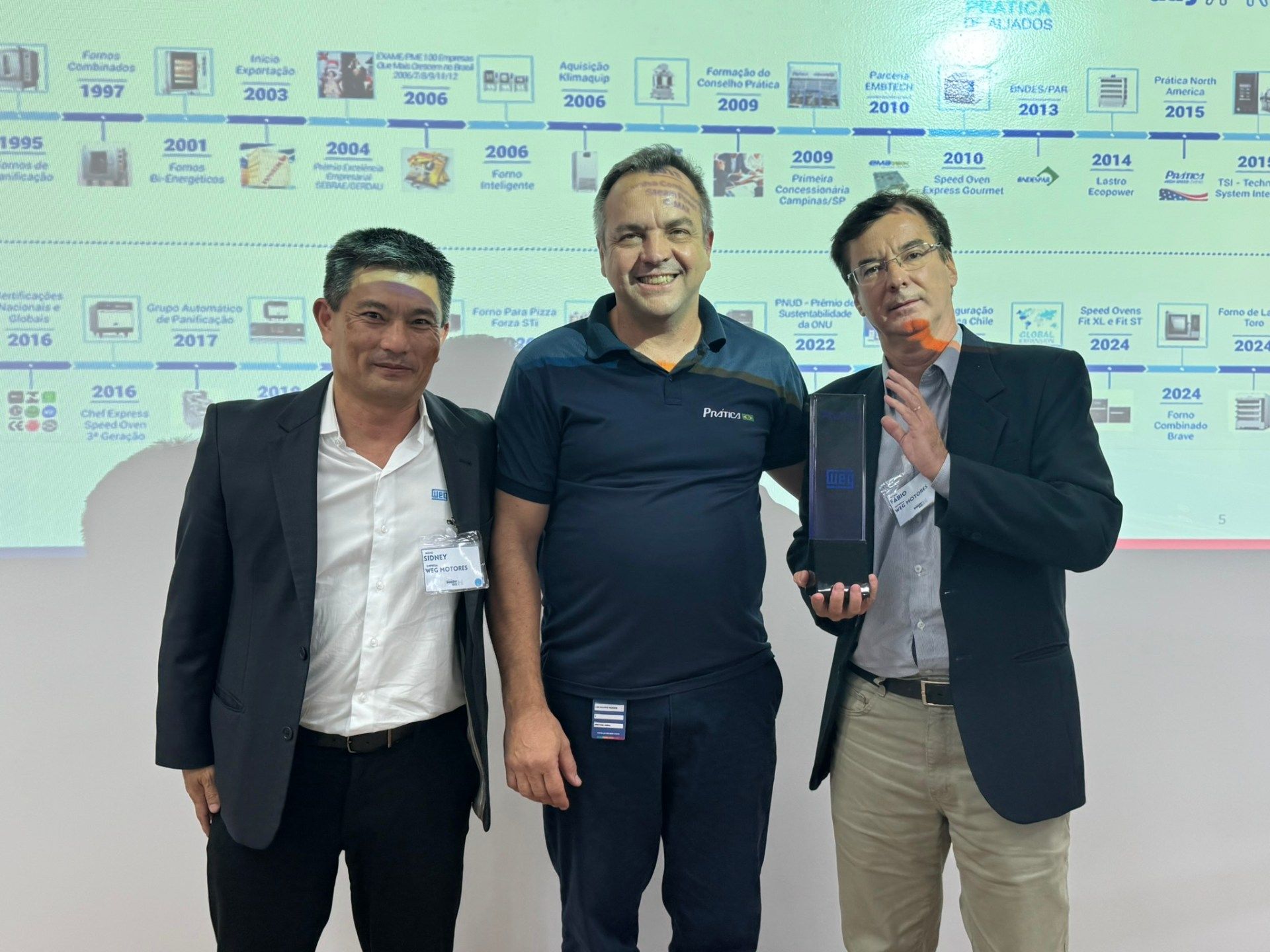 Três homens estão posando para uma foto em frente a uma linha do tempo.