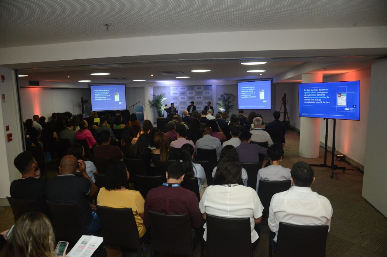 Um grande grupo de pessoas está sentado em uma sala assistindo a uma apresentação