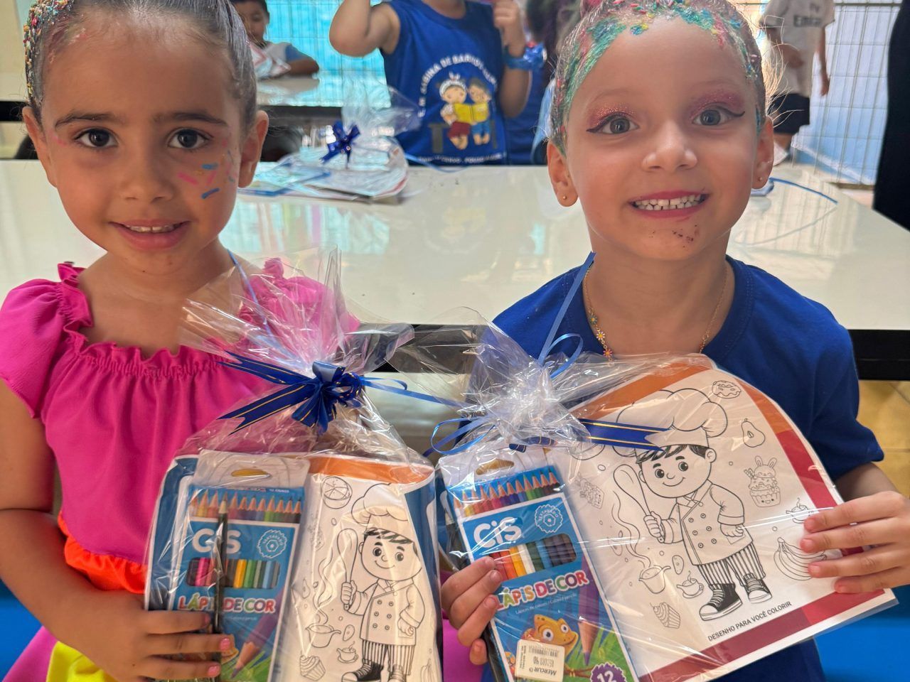 Duas meninas estão segurando presentes embrulhados em plástico e sorrindo.