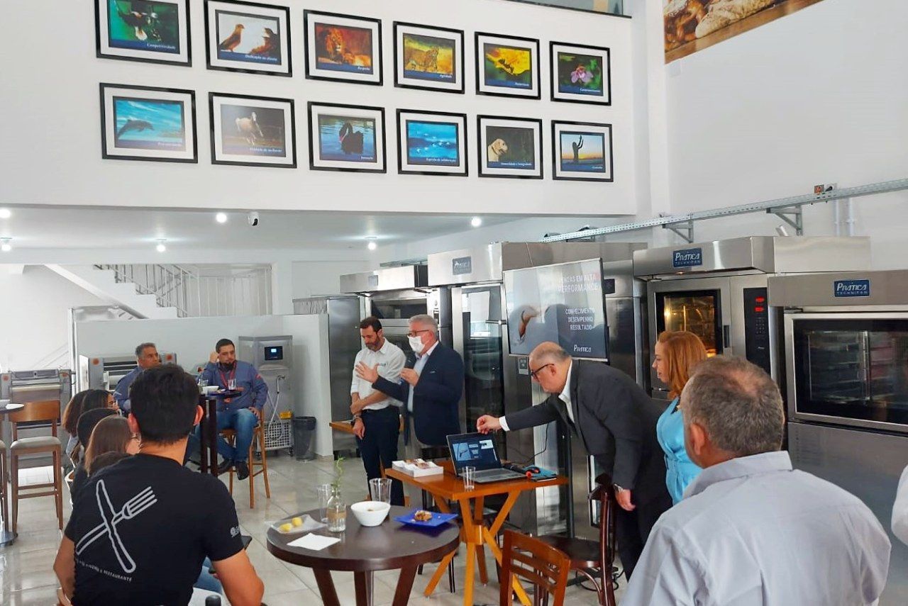 Um grupo de pessoas está sentado em mesas em uma sala com fotos na parede.