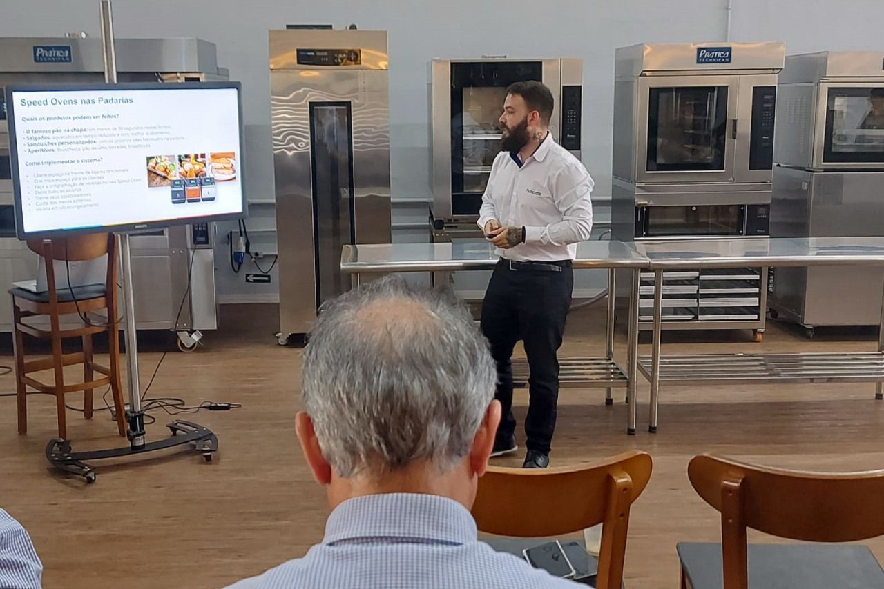 Um homem está fazendo uma apresentação para um grupo de pessoas em uma cozinha.