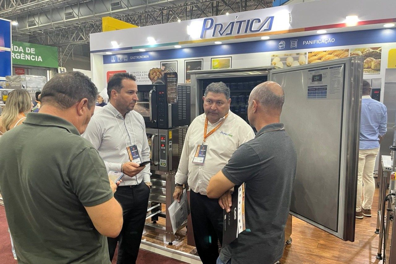 Um grupo de homens está em frente a um estande em uma feira comercial conversando entre si.