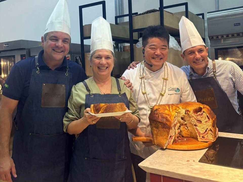 Um grupo de chefs estão de pé, um ao lado do outro, segurando um pedaço de pão.