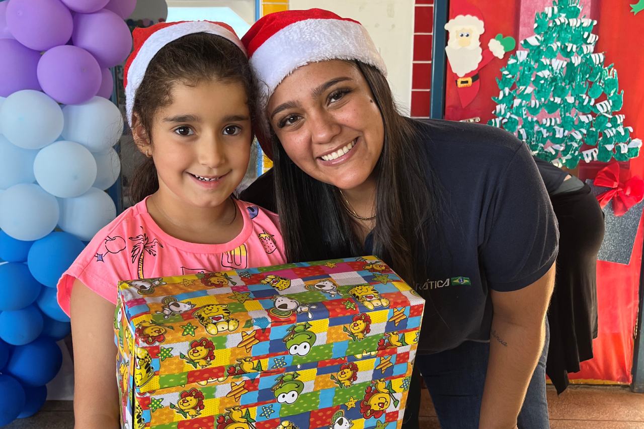 Uma mulher e uma menina usando chapéus de Papai Noel estão segurando uma caixa de presente.