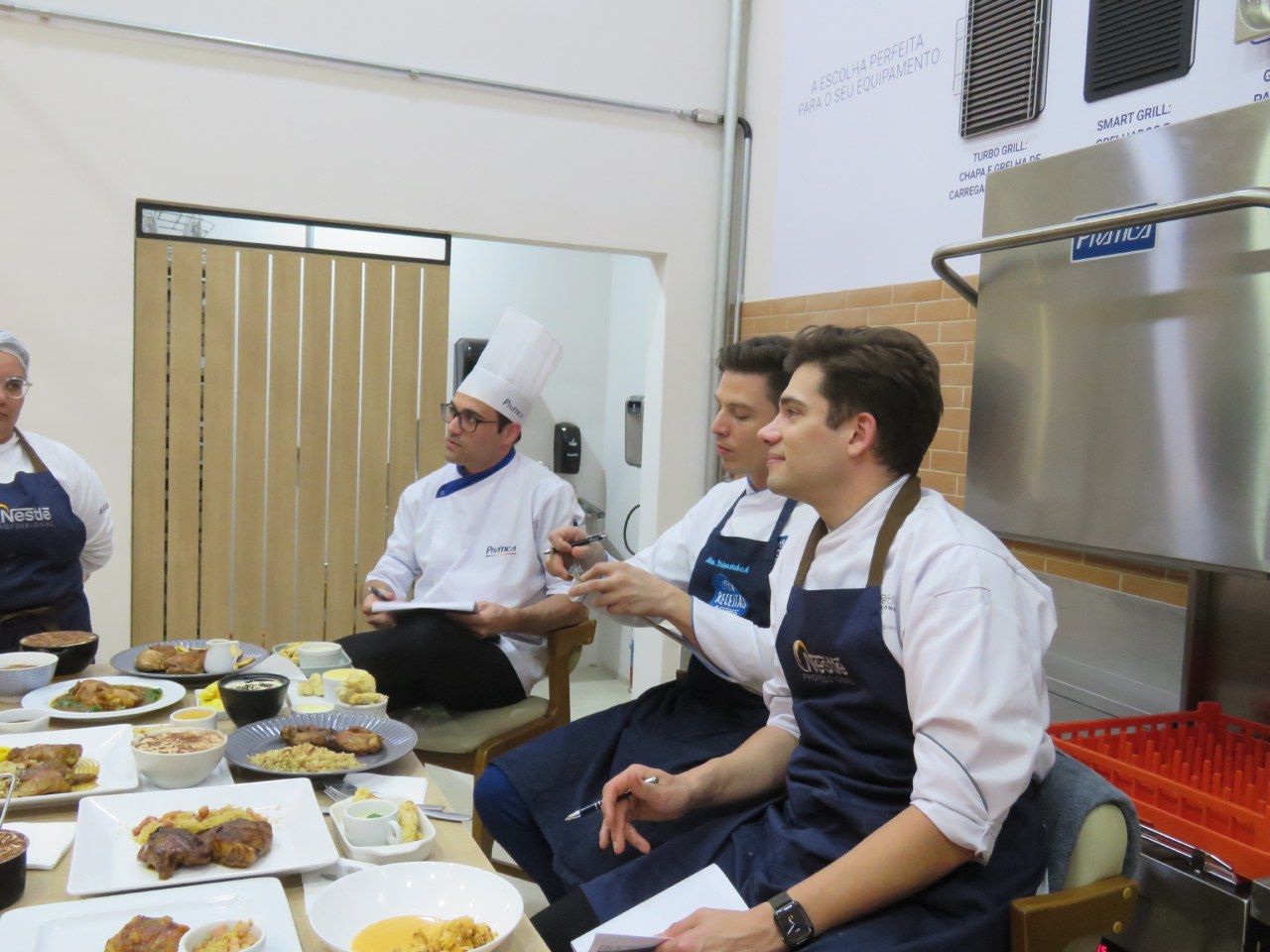 Um grupo de chefs estão sentados à mesa com pratos de comida