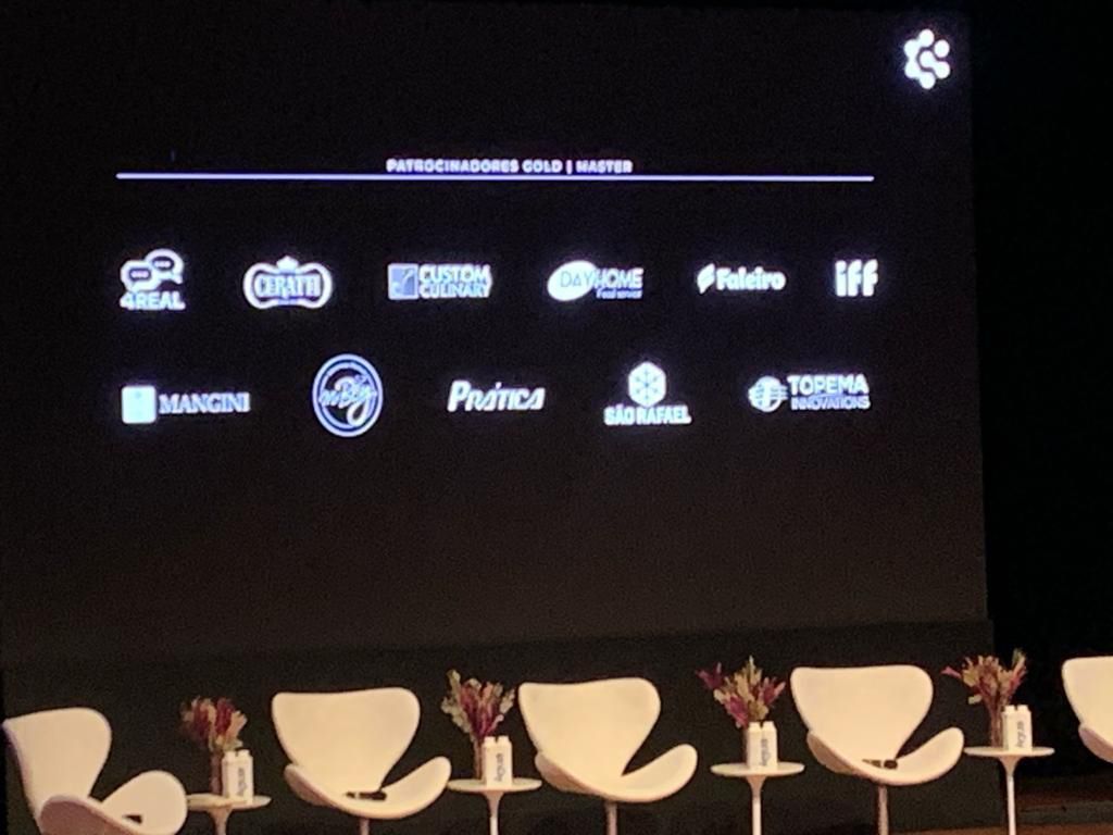 Uma fileira de cadeiras em frente a uma tela grande com logotipos nela