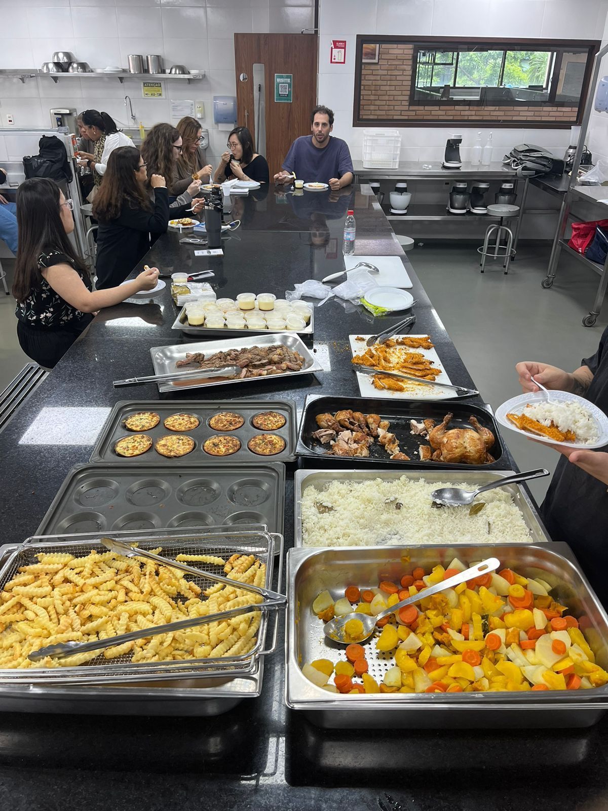 Um grupo de pessoas está sentado à mesa comendo comida de um bufê.