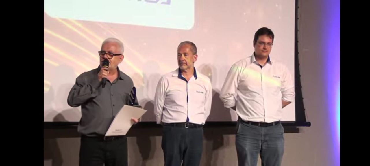 Três homens estão em pé na frente de uma tela de projetor.