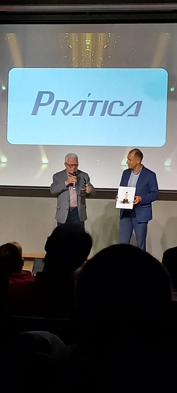 Dois homens estão em pé diante de uma tela grande com a palavra pratica escrita nela.