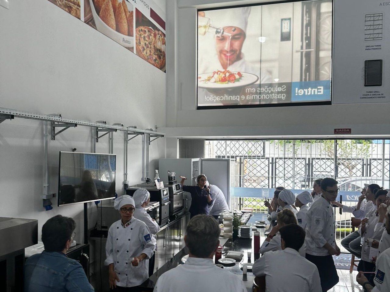 Um grupo de pessoas está sentado em frente a uma tela grande com um chef nela