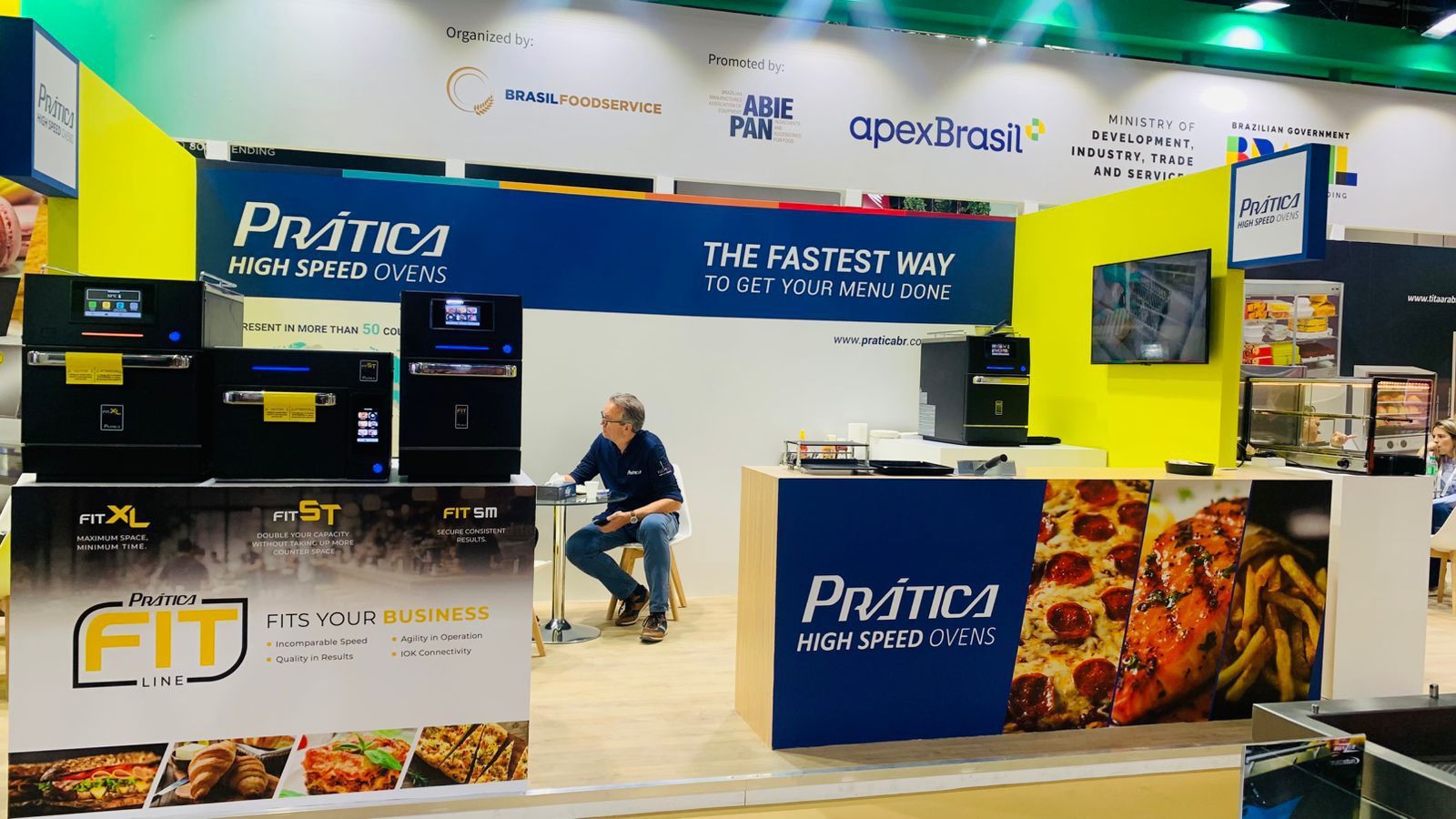 Um homem senta-se à mesa em frente a uma placa que diz pratica