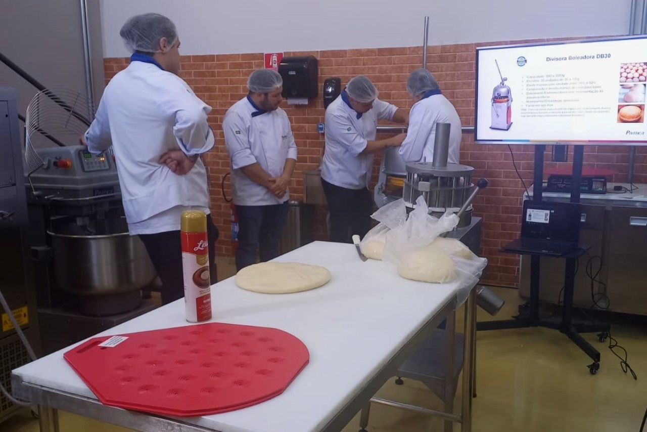 Um grupo de pessoas está em pé ao redor de uma mesa na cozinha.