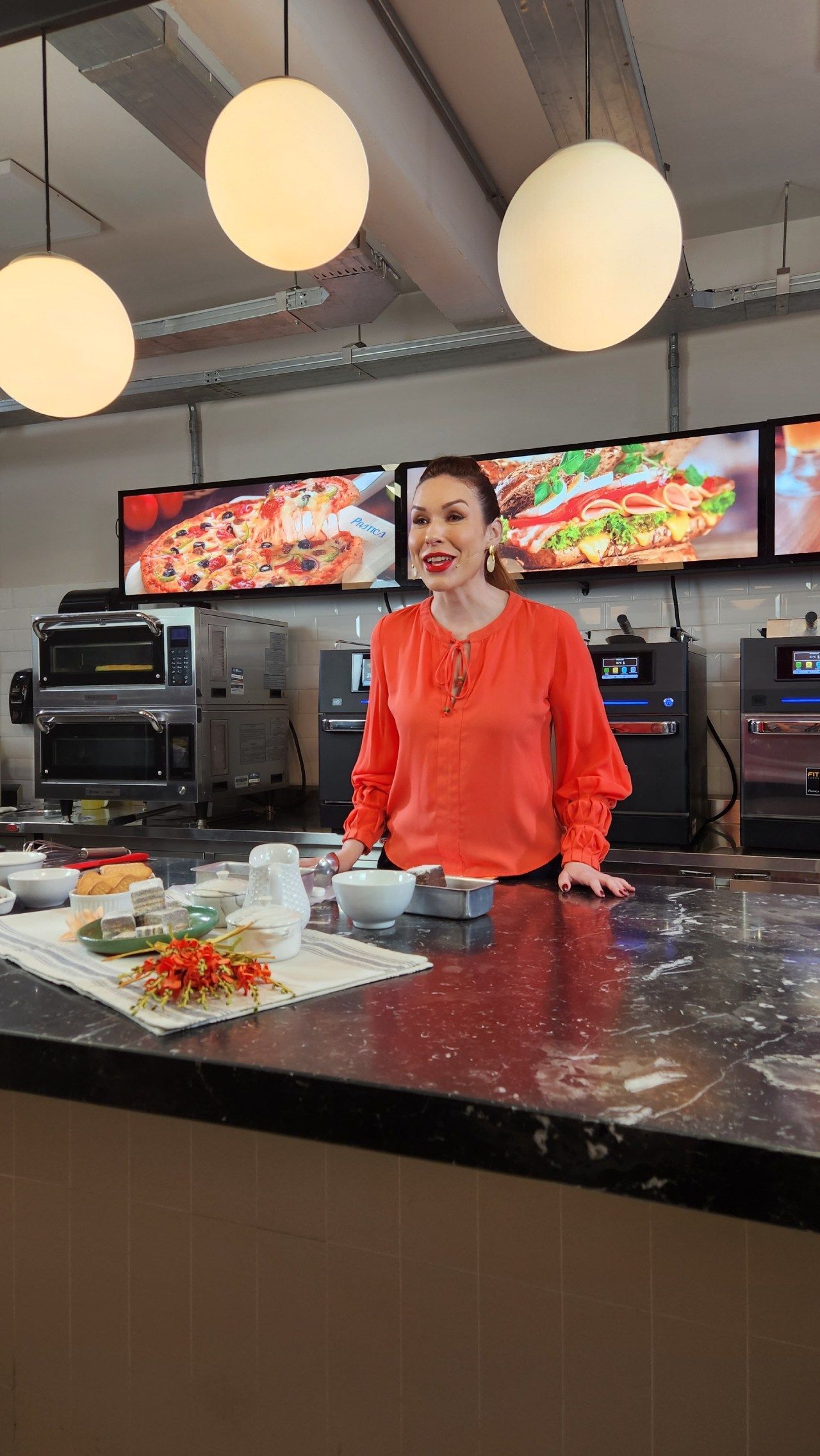 Uma mulher de camisa vermelha está parada em um balcão de cozinha.