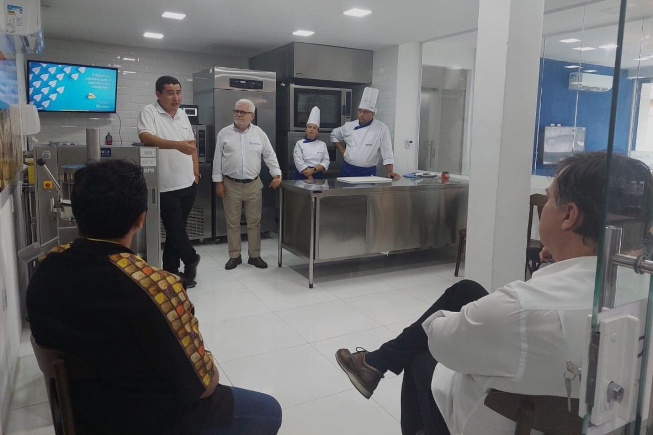 Um grupo de pessoas está sentado em uma sala com chefs ao fundo.